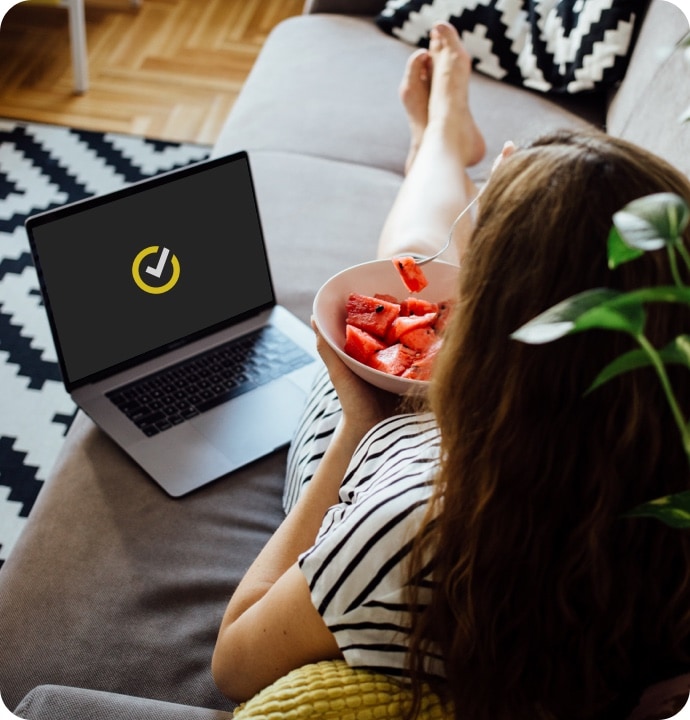 Mädchen auf dem Sofa mit Wassermelone und Laptop beim Starten von Norton 360 AntiVirus Plus